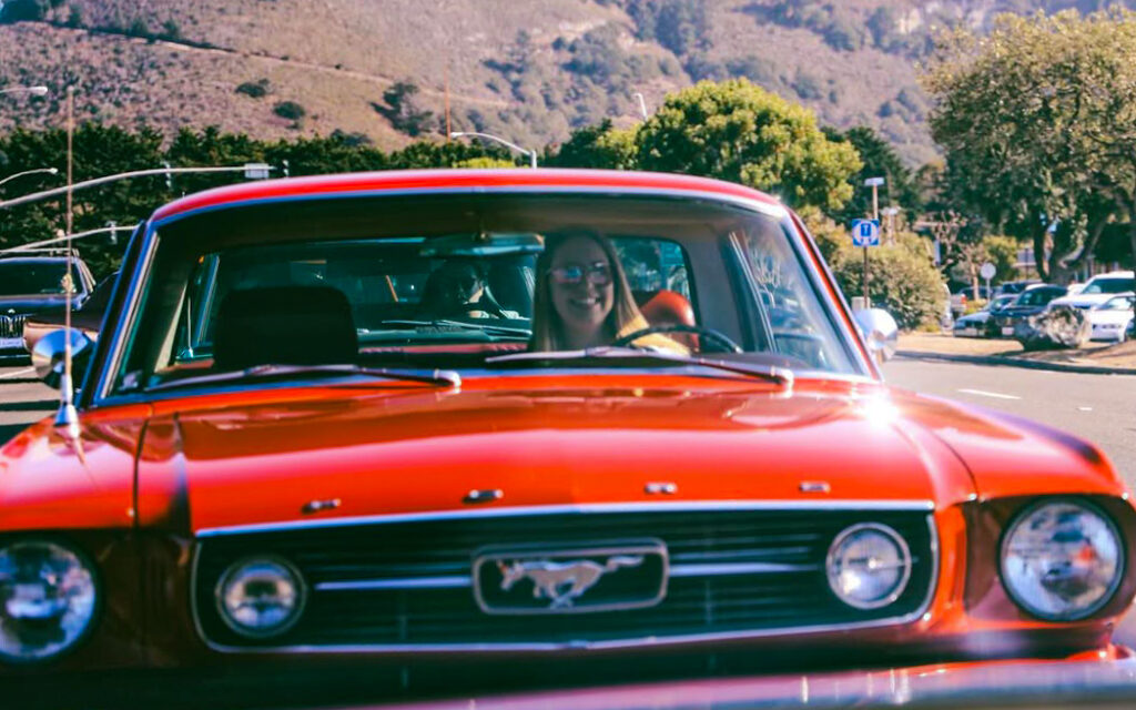 Francesca driving her 1966 Ford Mustang coupe on a California road