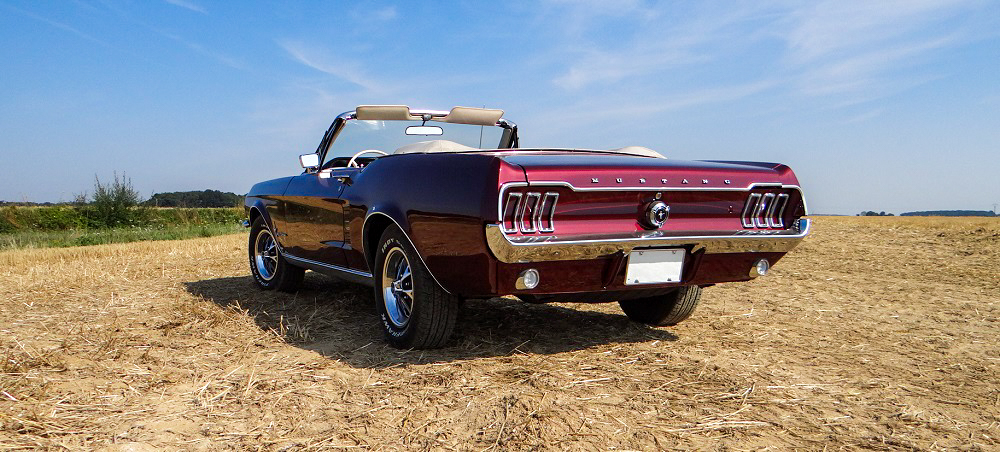 Rear view of a 1967 Mustang Convertible Vintage Burgundy in a wheat field, showcasing classic Mustang rear styling