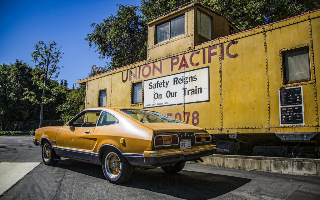 Rear view of yellow Mustang II Mach 1 near Union Pacific train