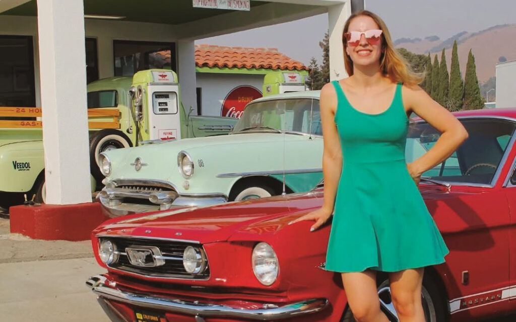 Francesca standing next to her 1966 Ford Mustang at a classic car event