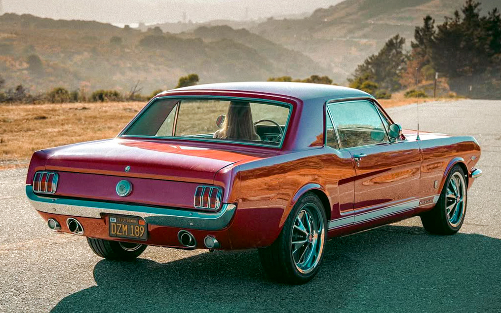 Rear view of Francesca driving her 1966 Ford Mustang on a California road