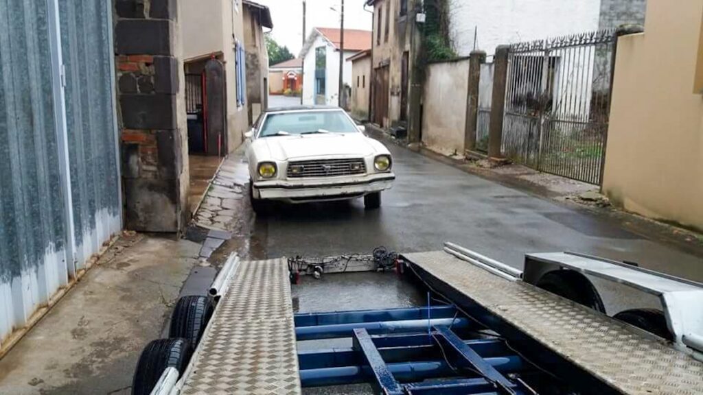 1975 Mustang II before restoration, original white paint, ready for transport on a flatbed truck