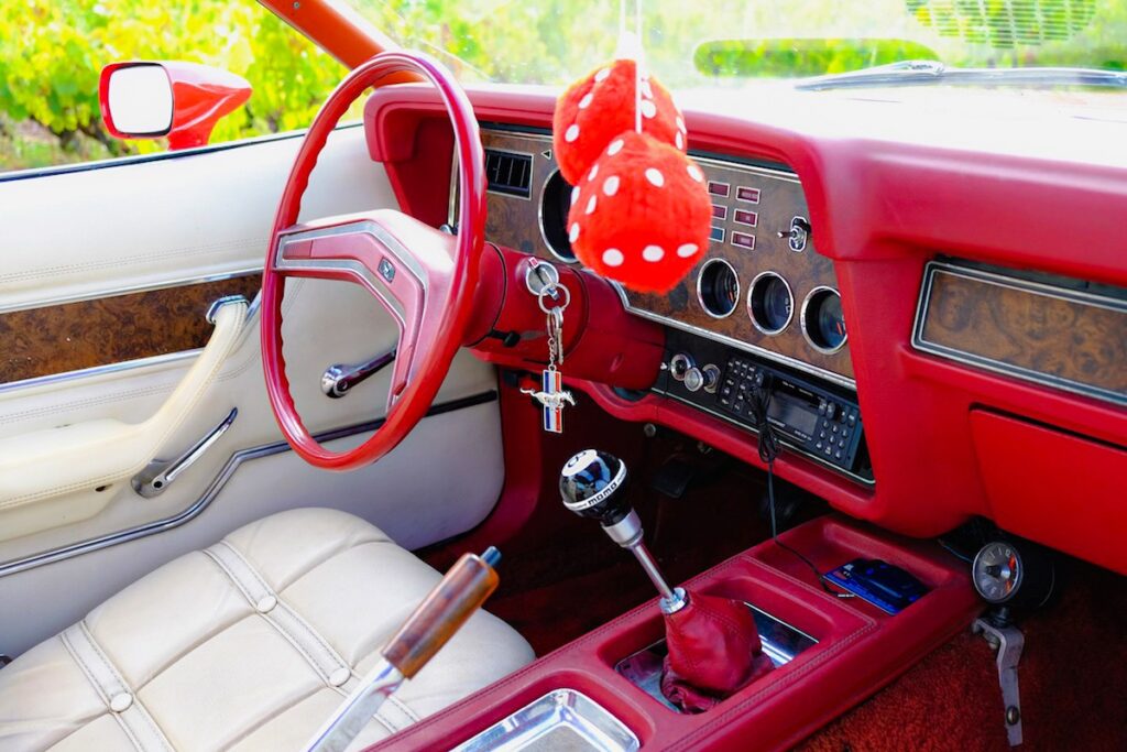 Interior of the 1976 Mustang II with red dice on the rearview mirror and an aftermarket gear knob, highlighting personal touches.